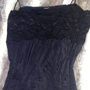 Svart topp med spetsdetaljer - Säljer en elegant svart topp med vacker spets upptill. Perfekt för en utekväll eller fest. Toppen har tunna axelband och har en tight passform som framhäver figuren. Materialet känns mjukt och bekvämt mot huden. Ett måste i garderoben för alla som älskar stilrena plagg! Köptes i England, lappen finns inte kvar så vet ej vad det är för märke.