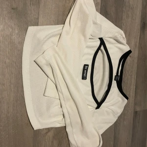 Vit ribbad topp från SHEIN - Snygg vit ribbad topp från SHEIN i storlek XS. Den har svarta kanter runt halsen och ärmlösa ärmar, vilket ger en stilren look. Perfekt för både vardag och fest!