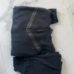 Svart hoodie och byxor från Nike - Säljer en svart hoodie och matchande byxor från Nike i storlek s. Hoodien har dragkedja och en klassisk design med huva. Perfekt för träning eller en avslappnad dag. Byxorna har en bekväm passform med dragsko i midjan.