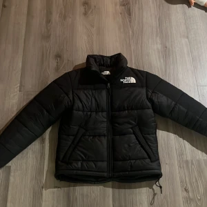 Svart dunjacka från The North Face - Säljer en svart dunjacka från The North Face i mycket bra skick. Jackan har en dragkedja framtill och är långärmad, perfekt för kalla vinterdagar. Den är både stilren och funktionell, med en klassisk design som passar till det mesta. Perfekt för dig som vill hålla värmen med stil! 🖤