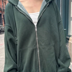 Brandy Melville zip-up hoodie  - En grön hoodie med dragkedja från brandy melville, knappt använd och i toppskick. Plagget är oversizes så de passar alla. Original pris 500kr