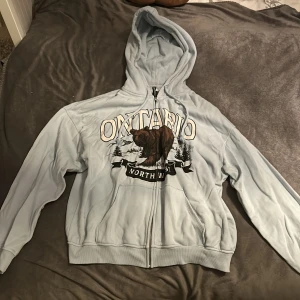 Blå kofta - En ljusblå hoodie med dragkedja, och ett tryck på där fram, knappt använd