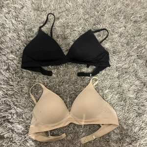 Två bh:ar i svart och beige - Säljer två bekväma bh:ar från Lindex i svart och beige. De har justerbara axelband och en enkel design utan mönster. Perfekta för vardagsbruk och ger bra stöd. Båda är i bra skick och redo för en ny ägare! Den svarta är använd väl medan den andra är använd nån gång bara. Köpte de för 300 något styck och säljer båda för 250 tillsammans, men kan gå ner i pris! Storleken är oklar för lapparna är bortklippta men jag är nästan helt säker på att båda är 75a eller 70a.
