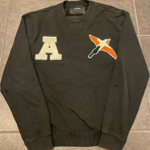 Svart tröja från Axel Arigato - Säljer en svart tröja från Axel Arigato med coola detaljer. Den har ett stort 'A' och en broderad fågel i orange, vit och svart på framsidan. Perfekt för höst och vinter, och den är i mycket bra skick. Passar till både vardag och fest! Skick 9 av 10 använd fåtal gånger. Storlek s herr. Nypris 1699 köpt på nk Stockholm. Priset är inte helt fast, det går att pruta. Bara att skriva ifall ni har frågor!