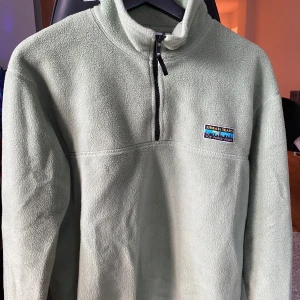 Grön fleece från Junkyard - Mysig ljusgrön fleece från Junkyard i storlek XS. Perfekt för kyliga dagar med sin halvdragkedja och hög krage. Den har en liten Urban Tears-logga på bröstet. Superbekväm och stilren för både vardag och chill. Tröjan är oversize, passar även storleks S.