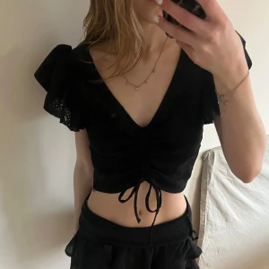 Svart topp med volanger - Super söt topp! Man kan reglera hur kort den ska vara, den har även en dragkedja på sidan🤍