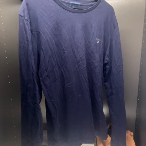 Mörkblå långärmad tröja från Gant - Säljer en stilren mörkblå långärmad tröja från Gant i slim fit. Perfekt för en avslappnad men ändå snygg look. Tröjan har en diskret logga på bröstet och är tillverkad i ett mjukt material.
