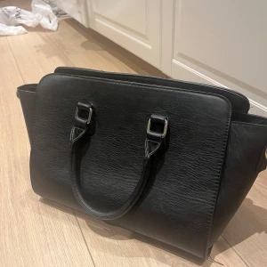 Svart handväska med dragkedja - Snygg svart handväska. Perfekt för att bära dina dagliga nödvändigheter. Stilren design med två handtag för enkel bärning.