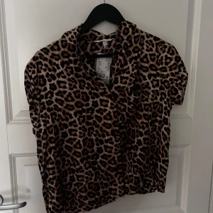 Leopardmönstrad blus - Säljer en trendig leopardmönstrad blus med korta ärmar. Perfekt för att ge din outfit en djärv touch. Blusen har en klassisk krage och är gjord i ett mjukt material som känns skönt mot huden.