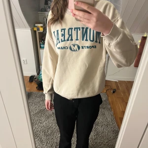 Beige sweatshirt med tryck - Säljer en beige sweatshirt med blått tryck 'Montreal Sports Champs'. Tröjan har långa ärmar och en avslappnad passform. Perfekt för en casual look.