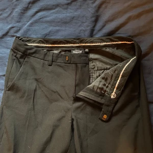 Low waisted svarta kostymbyxor från KappAhl - Snygga svarta kostymbyxor från KappAhl med dragkedja och knappstängning. Byxorna har en klassisk design med fickor fram och bak, perfekta för en stilren look. Den är inte använd utan bara bara rullas lite.