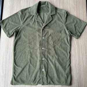 Olivgrön frottéskjorta från John Henric - Säljer en olivgrön kortärmad skjorta från John Henric i frotté. Skjortan har en klassisk krage och knappar framtill. Perfekt för en avslappnad stil.