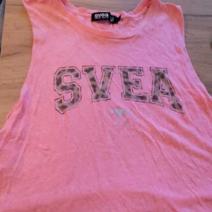 Rosa linne från Svea - Säljer ett rosa linne från Svea med stort tryck på framsidan. Perfekt för varma dagar eller som ett lager under en jacka. Linnet har en avslappnad passform och är gjord i ett mjukt material.