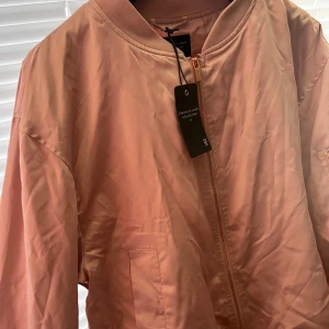 Rosa bomberjacka från The Black Label Collection - Snygg rosa bomberjacka från The Black Label Collection med dragkedja framtill och en praktisk ficka med dragkedja på ärmen. Perfekt för en stilren look.