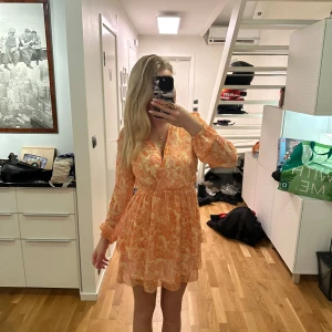 Orange blommig klänning från Amisu - Säljer en söt orange blommig klänning från Amisu i storlek 34. Klänningen har långa ärmar och en v-ringad design med volangdetaljer. Perfekt för en somrig look! 🌸