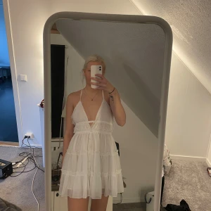 Vit klänning från ASOS DESIGN - Säljer en söt vit klänning från ASOS DESIGN med spetsdetaljer och volanger. Klänningen har en djup v-ringning och smala axelband som korsas i ryggen. Perfekt för sommarens varma dagar och till studenten!