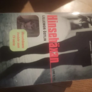Hinsehaxan - Boken 'Hinsehaxan' av Lillemor Östlin är en fascinerande berättelse som även blivit en TV-serie. Omslaget har en dramatisk design med titeln i röd text och en bild av en person i skugga.