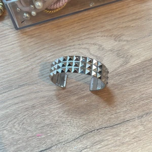 Silvrigt armband med nitar - Snyggt och trendigt armband i silver med nitar. Perfekt för att ge din outfit en edgy touch. Armbandet är öppet och justerbart för att passa de flesta handleder.