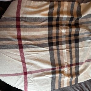 Rutig halsduk i beige och svart - Snygg rutig halsduk i beige, svart och vinrött. Perfekt för att hålla sig varm och stilren under kyliga dagar. Den har ett klassiskt rutmönster som ger en tidlös look.