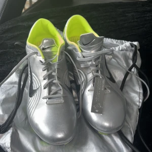 Silverfärgade fotbollsskor från Nike limited edition  - Snygga silverfärgade fotbollsskor från Nike med neongula detaljer och svart logotyp. Skorna har snörning och en modern design som sticker ut på planen. Perfekta för den som vill ha stil och funktion i ett. Finns bara 4500 par i världen. Har kvittot på skorna. Storlek 44,5