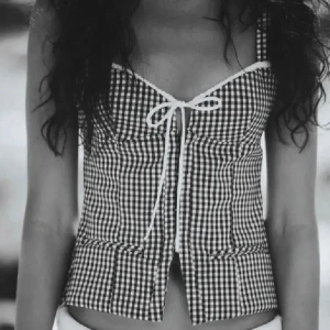 Svartvit rutig korsett - Snygg svartvit rutig korsett med knytning framtill. Den har smala axelband och en figurnära passform som ger en stilren look. Använd 1 gång!