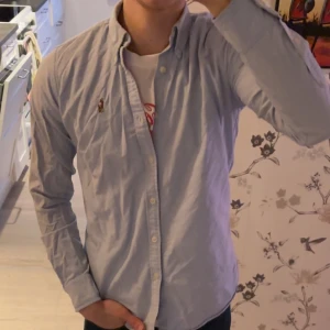 Ljusblå skjorta från Ralph Lauren - Snygg ljusblå skjorta från Ralph Lauren med klassisk krage och broderad logga på bröstet. Använd ca 6-7 gånger. Den är Slim fit och passar Xs men fungerar bra även om man är kortare som en regular.
