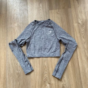Grå croppad tröja från Gymshark - Snygg grå croppad tröja från Gymshark i ett mjukt och stretchigt material. Perfekt för träning eller en avslappnad look. I mycket bra skick💓