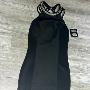 Svart klänning med pärldetaljer från Nelly One - Elegant svart klänning med pärldetaljer runt halsen och smala axelband. Perfekt för en kväll ute. Klänningen har en figurnära passform och är tillverkad i ett mjukt material som ger en lyxig känsla. Prislapp är kvar på!