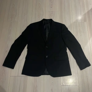 Svart kavaj från H&M - Snygg svart kavaj från H&M i slim fit. Perfekt för en stilren look. Kavajen har två knappar framtill och är tillverkad i ett elegant material som ger en klassisk känsla. Kavajen har storlek L, stilren och väl värt pengarna ✅