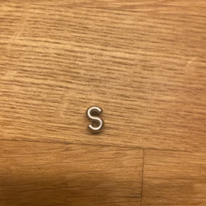 Silverberlock med bokstaven S - Charmig silverberlock formad som bokstaven S. Ena sidan är slät medan den andra är dekorerad med små hjärtan.
