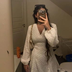 Vit blommig sommarklänning  - Charmig vit  från Divided med små blommor. Klänningen har en knytning i midjan för så man kan dra åt för perfekt passform. Perfekt för en somrig look! Den ha blivit lite missfärgad (pga smycken) vid kragen bak på klänningen men d inget som syns när man ha på sig