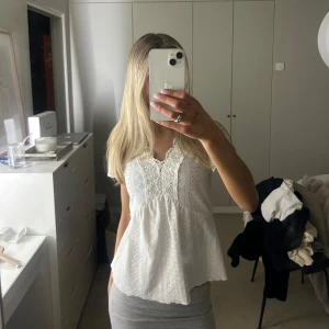 Vit ärmlös blus - Säljer en söt vit ärmlös blus med spetsdetaljer. Blusen har en luftig passform. I story XS