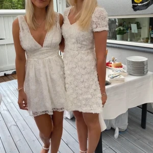 Vit spetsklänning med v-ringning - Säljer en vacker vit spetsklänning med djup v-ringning och ärmlös design. Klänningen har en elegant passform och är perfekt för sommarens festligheter. Den har en kort längd och ett fint spetsmönster som ger en romantisk känsla. Klänningen är helt ny från showpo, nypris ca 1600. Skulle säga att klänningen är i stolek S.