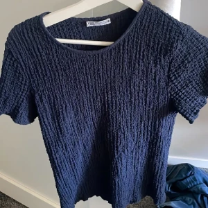 Mörkblå ribbad topp från Zara - Säljer en mörkblå ribbad topp från Zara. Den har en rund halsringning och korta ärmar. Perfekt för en stilren och bekväm look.
