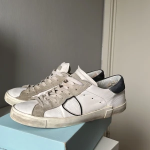 Vita sneakers från Philippe Model - Snygga vita sneakers från Philippe Model med grå och svarta detaljer. Skorna har snörning och en stilren design som passar perfekt till vardags. De är tillverkade i skinn och har en bekväm passform. Dom är ganska slitna där bak och på insidan men funkar hur bra som helst. Säljer dom på grund av att dom är för små. Nypris: 3200kr                                                               Box medföljer 