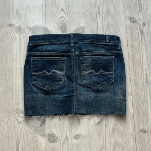 Mörkblå lågmidjad jeanskjol från 7 For All Mankind - Mörkblå lågmidjad jeanskjol från 7 For All Mankind som jag har gjort om från en längre kjol. Fint skick. Storlek 28. Tvärs över midjan är det ca 39 cm + stretch och längs med sidan är det 33 cm. Använd gärna köp nu!