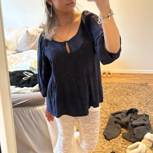 Mörkblå blus med trekvartsärm - Säljer en elegant mörkblå blus med trekvartsärm och en liten knappdetalj framtill. Blusen har en luftig passform och är perfekt för både vardag och speciella tillfällen. Den är tillverkad i ett mjukt och bekvämt material. Storlek 42 men sitter fint på mig som är en XS/S