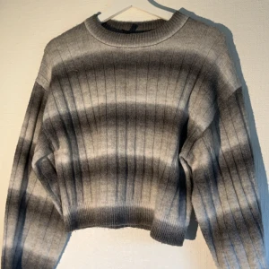 Grå ribbad tröja från Devided  - Säljer en snygg grå ribbad tröja från Devided. Tröjan har ett stilrent mönster med skiftande grå nyanser och långa ärmar. Perfekt för kyligare dagar! Knappt använd!