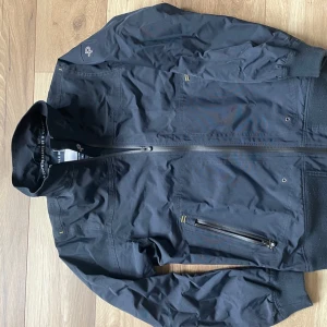 PelleP jacka  - Säljer en stilren mörkblå vindjacka från PelleP. Jackan har en dragkedja framtill och praktiska fickor med dragkedjor. Perfekt för blåsiga dagar och har en modern look. Passar bra till både vardag och äventyr. Nypris runt 3000. Inga tecken på användning. 