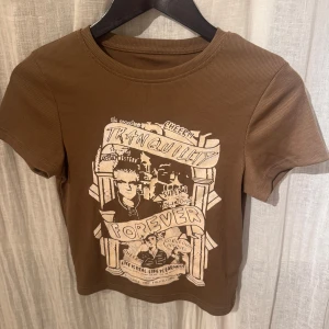 Brun t-shirt med tryck - Snygg brun t-shirt med ett coolt tryck på framsidan. T-shirten har en ribbad struktur och korta ärmar, perfekt för en avslappnad stil.