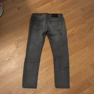 Grå jeans från Jacob Cohen - Snygga grå jeans från Jacob Cohen med klassisk femficksdesign. De har en knappgylf och stilrena sömmar. Perfekta för en avslappnad men stilren look. Storlek 31. Passar de som är runt 175. Nypris 5000.