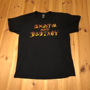 Svart t-shirt från Thrasher - Cool svart t-shirt från Thrasher med texten 'Skate and Destroy' i röd och gul färg på framsidan. Perfekt för skate-entusiaster som vill ha en avslappnad stil.