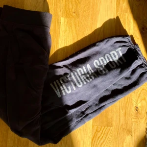 Mörkblå mjukisbyxor från Victoria Sport - Mörkblå supersköna mjukisbyxor från Victoria Sport. Byxorna har en något lösare passform och ca en dm korta för mig som 177cm. Victoria Sport tryck i ljusblå/grå färg längs baksidan av ena benet.
