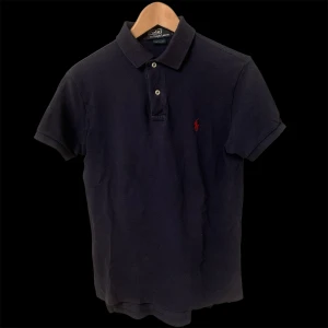 Svart pikétröja från Ralph Lauren - Säljer denna marinblåa custom fit Ralph lauren pikén till dig som vill ha nåt skönt till sommaren. Den är i storlek s (160+) och är stretchig. Den är i bra/okej skick på grund av att den är använd 5-10 gånger, legat i en oöppnad Zalando påse som har varit i garderoben i 5 månader och har två söndriga sömnar på under delen av pikén. Men det går att sy fast eller att bara vika upp den. Det har jag gjort när jag har använt den. Pikén är en gammal model och funkar perfekt. Tveka inte om att skriva. 