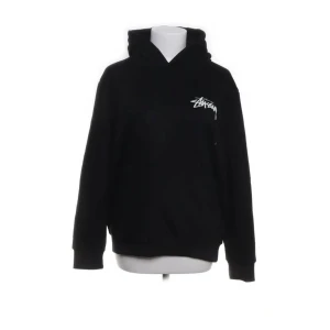 Svart hoodie från Stussy - Säljer en svart hoodie från Stussy med tryck på både fram- och baksida. Framsidan har en liten vit logga medan baksidan har en stor färgglad design med olika städer. Perfekt för en streetwear-look!