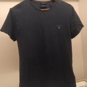 Mörkblå t-shirt från GANT - Säljer en stilren mörkblå t-shirt från GANT i storlek XS. T-shirten har en liten broderad logga på bröstet och är tillverkad i mjukt material. Perfekt för en avslappnad look.