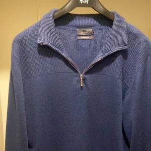 Mörkblå stickad tröja med dragkedja - Säljer en mörkblå stickad tröja från H&M med dragkedja och krage. Perfekt för kyliga dagar med sin mysiga och stilrena design. Tröjan har långa ärmar och en texturerad yta upptill.