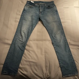 Levis 512 jeans i ljusblå denim - Snygga Levis 512 jeans i ljusblå denim med en klassisk femficksdesign. De har en dragkedja och knapp framtill samt en läderpatch med Levis-logga på baksidan. Perfekta för en avslappnad stil.