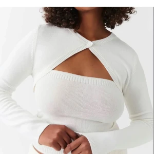 Vit ribbad bolerotopp - Snygg vit ribbad bolerotopp med långärmad design. Perfekt för att lägga till en stilren touch till din outfit. Den har en unik öppning framtill som ger en modern look. Slutsåld överallt ‼️