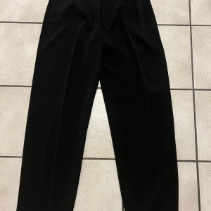 Svarta kostymbyxor från Solon storlek 28, midja 72 cm - Snygga svarta kostymbyxor från Solon med en klassisk design. Byxorna har en dragkedja och är högmidjade för en elegant look. Perfekta för en stilren outfit.